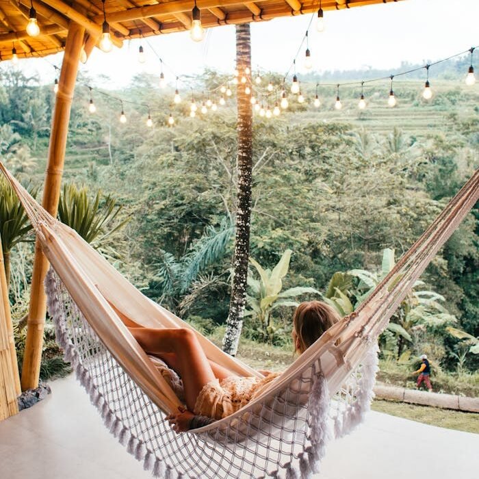 Woman resting in hammock under glowing garlands surrounded by trees and nature.